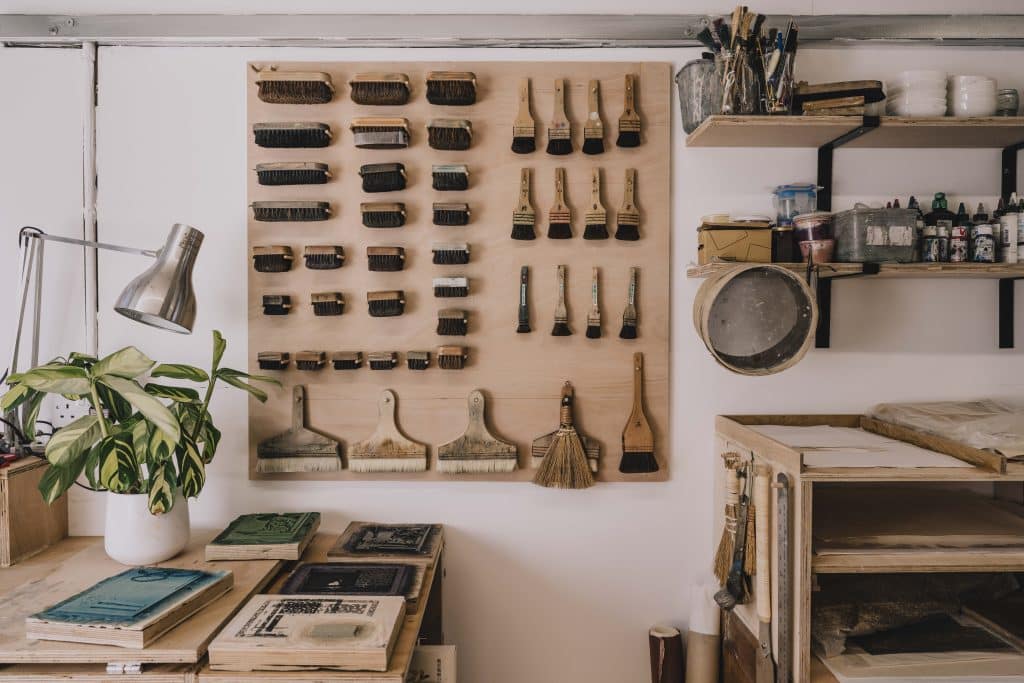 Interior view of a creative workshop with tools neatly arranged on a pegboard and a workbench, alongside an exterior shot of the Krowji arts centre showing modern classroom buildings, courtyard, and surrounding greenery in Cornwall