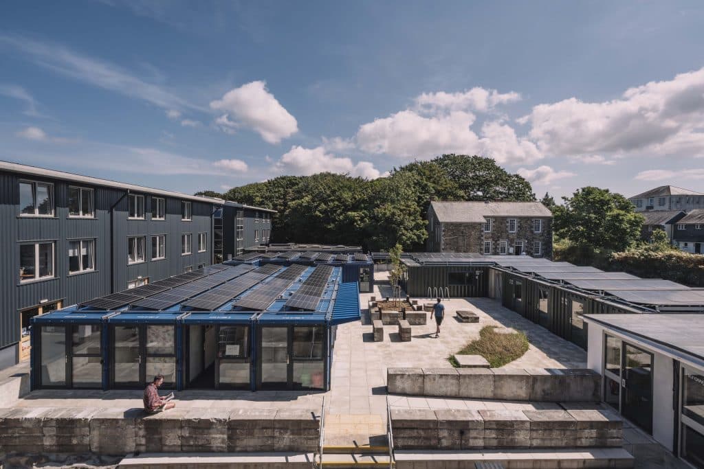 Exterior view of a multi-window institutional building with a courtyard, surrounded by trees under a partly cloudy sky.